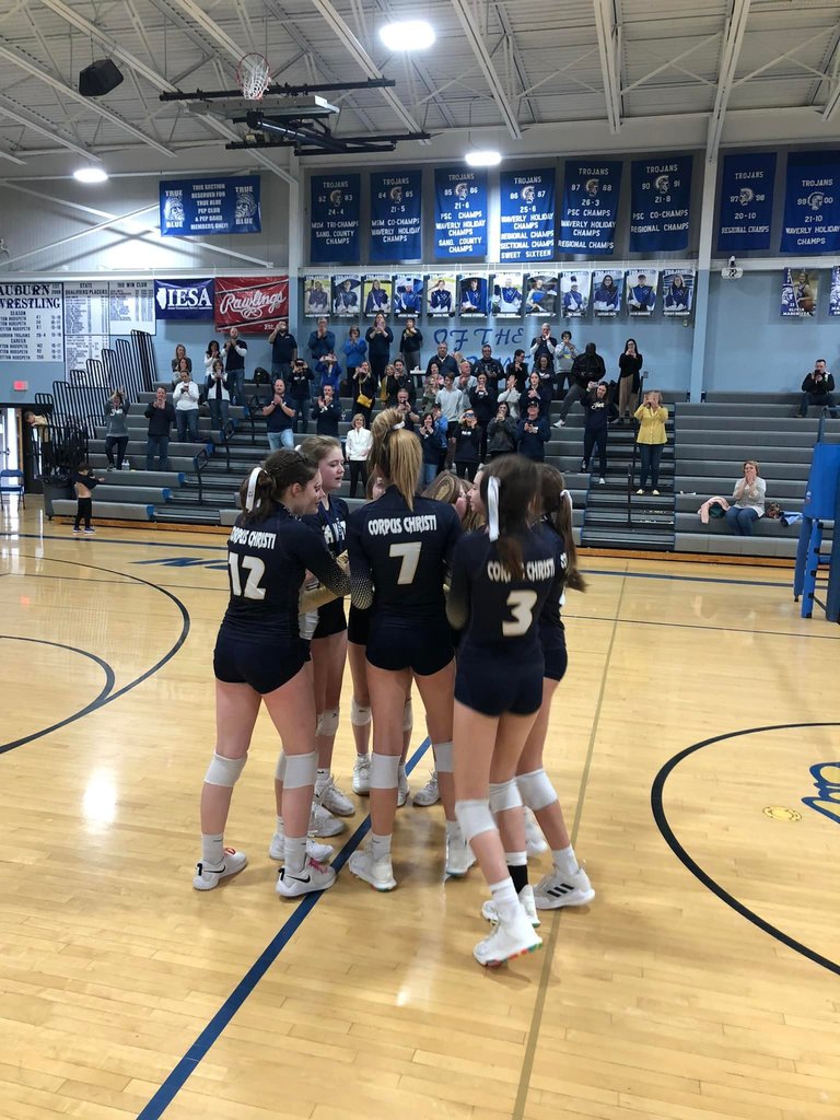 girls volleyball team in blue jerseys in a huddle on the volleyball court