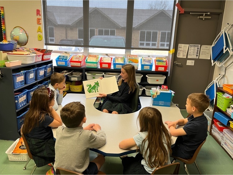 older student sitting at u-shaped desk reading to younger students