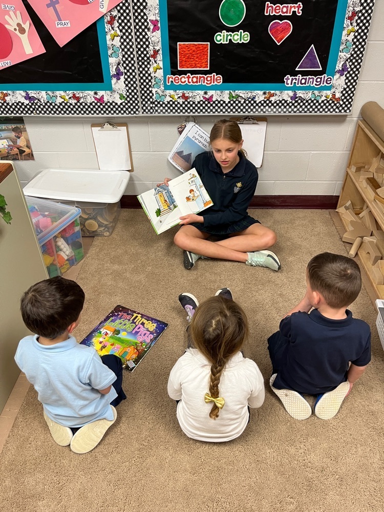 older student reading to three younger students at carpet